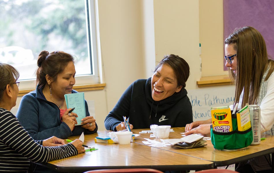 Small group of adults seated around a table collaborating on an activity, reviewing notes and cards with classroom materials visible.